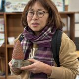 モルタルアート作品の小さな家を手に持ち、微笑む女性参加者。室内のレッスン会場で撮影された一枚。