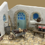 白い漆喰壁と石畳を表現したモルタルアートのミニチュアガーデン作品。小物や植物を組み合わせ、物語を感じさせる庭の一角を再現している。