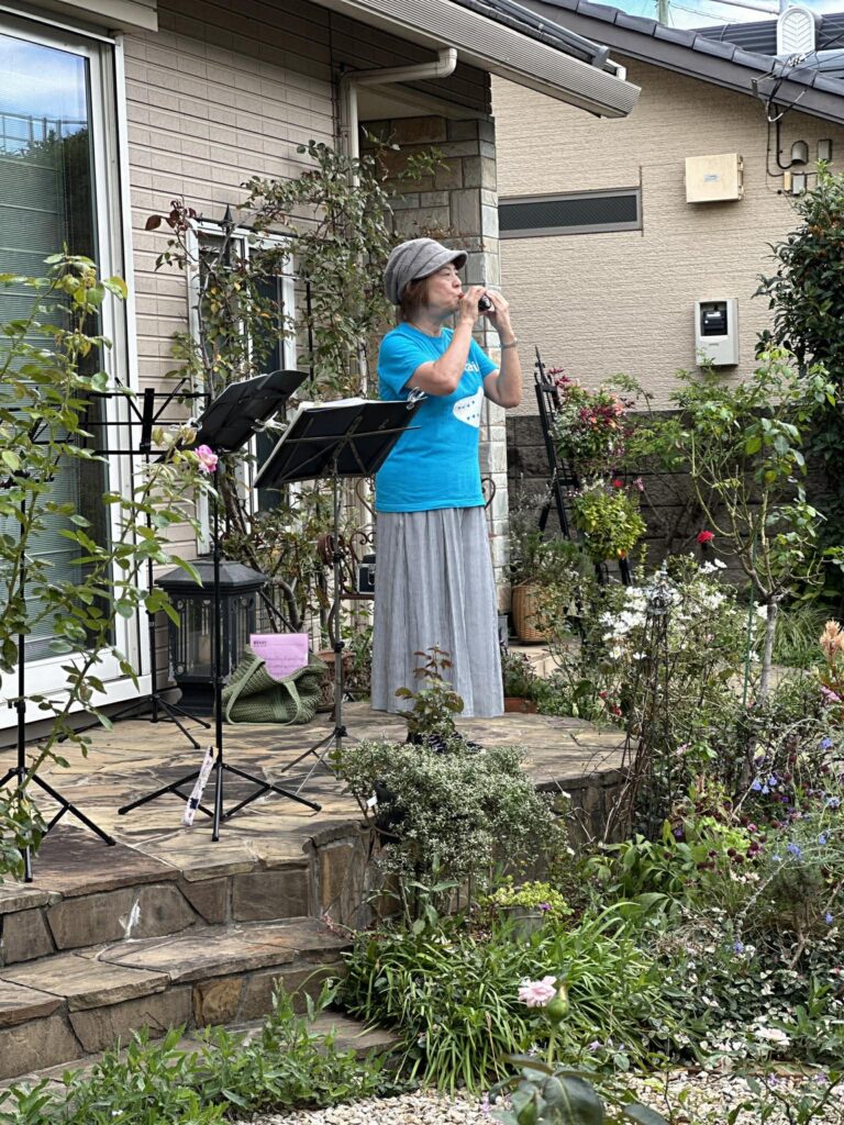 色とりどりの花が咲くガーデンのテラスで、女性がオカリナを演奏しているイベントの様子