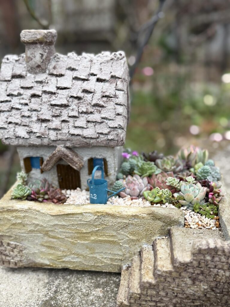 小さな家のミニチュアと多肉植物が組み合わされたナチュラルなガーデン風アレンジ