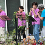 庭の花々に囲まれたテラスで女性たちがオカリナ演奏を行っている様子