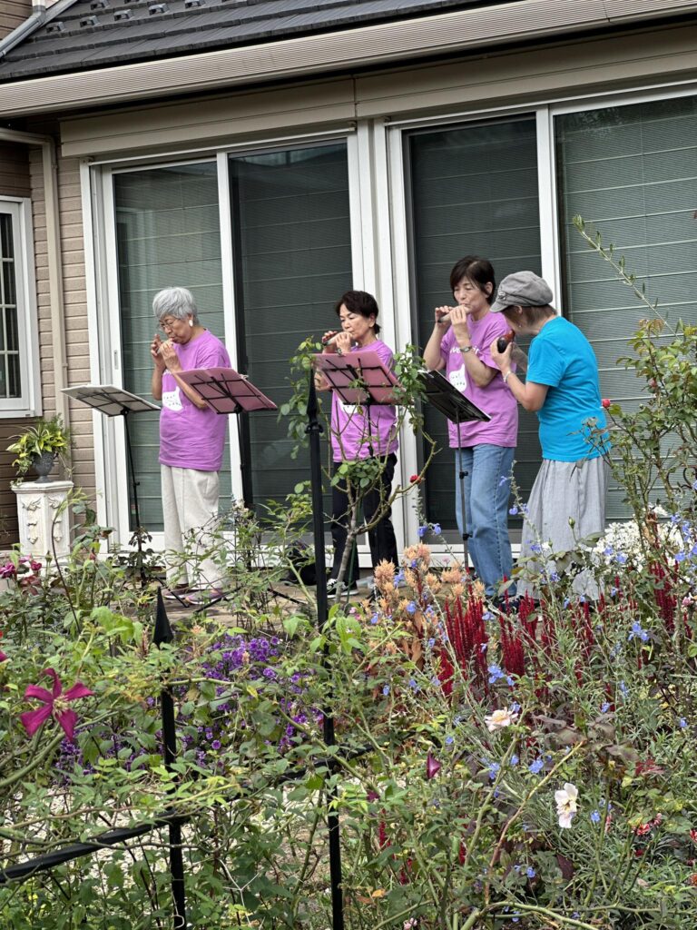 庭の前で楽譜を見ながらオカリナを演奏する女性グループの様子
