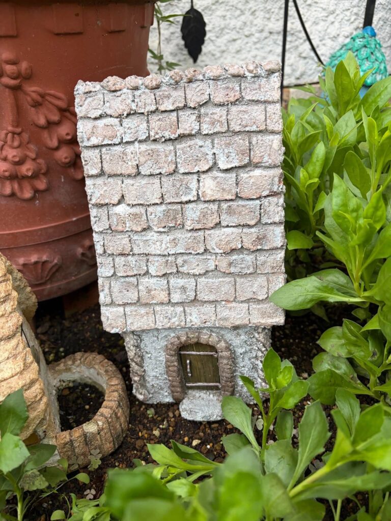 植物の中に置かれたレンガ造り風の小さな家のガーデンオブジェ