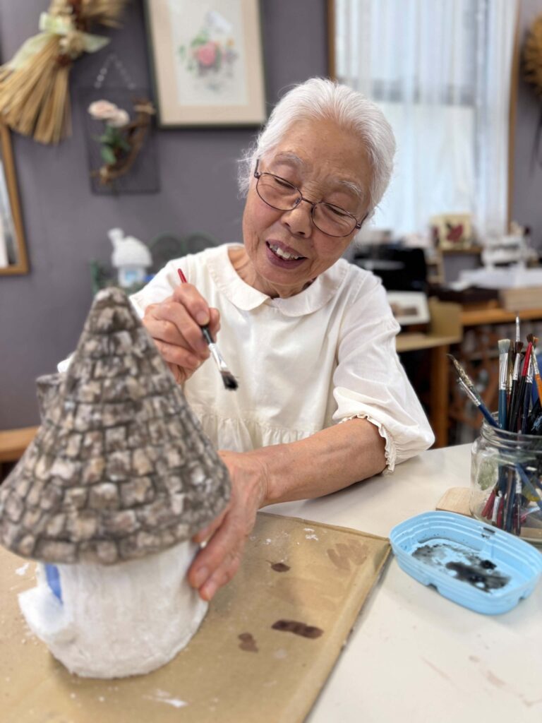 筆を使って、とんがり屋根のモルタルアートの家に色を塗る女性